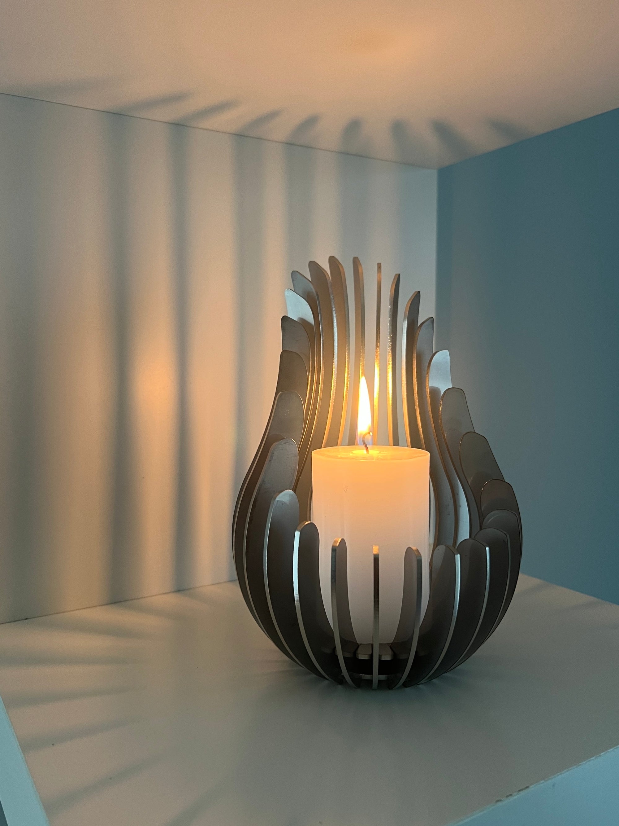 Kelray stainless steel candle holder with lit pillar candle casting decorative shadows on a white shelf.